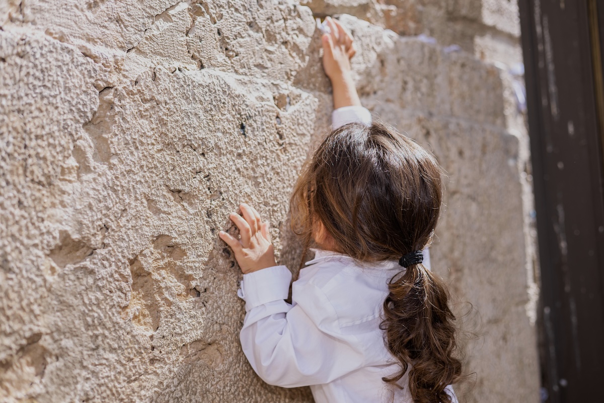 ילד עם שיער ארוך נוגע באבני הכותל המערבי – טקס חלאקה מסורתי בירושלים עם כינור דוד